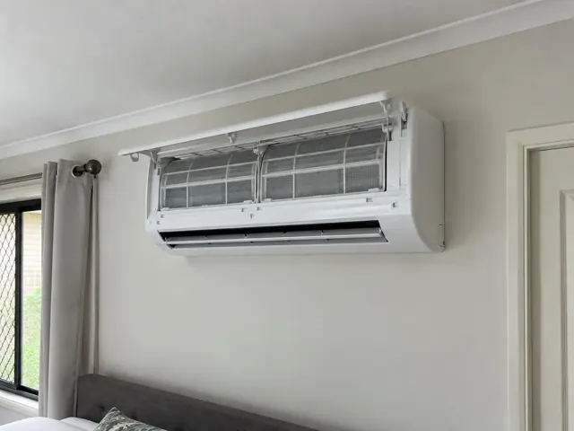 Wall-mounted split system with open front panel and clean filters on a light interior wall in Upper Coomera