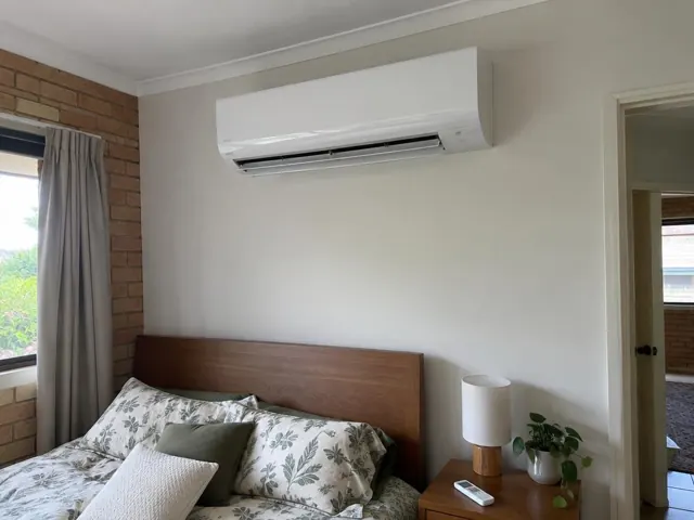 White split system above a bed in a brick-and-plaster bedroom in Ormeau