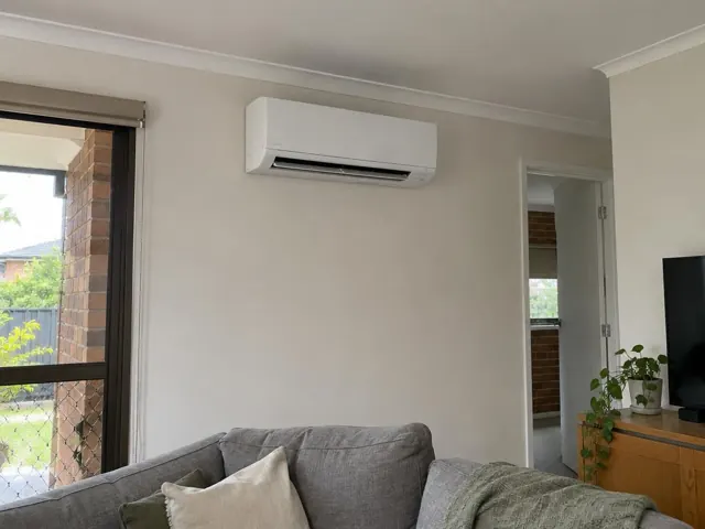 Wall-mounted split system above a sofa in a light living room with tiled doorway in Coomera
